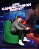 A man is playing a video game while sitting on a green beanbag chair in a dimly lit room with gaming equipment. Produktbild-Vorschau