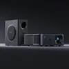 A black projector and a black subwoofer are displayed on a dark surface against a black background. Náhled obrázku produktu