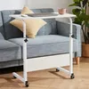 A white laptop table with adjustable height and wheels is placed next to a sofa, with a laptop, mouse, and a mug on it. Anteprima dell’immagine prodotto