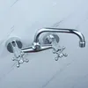 A chrome-plated wall-mounted faucet with two handles and a U-shaped spout is mounted on a marble-patterned wall. Produktbild-Vorschau