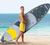A man holding a paddleboard on a beach with the ocean in the background. Náhled obrázku produktu
