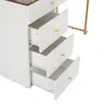 A close-up view of a white dresser with three open drawers, each with a gold knob. The top drawer is slightly ajar, revealing the interior. The dresser is part of a larger vanity set, with a gold metal leg visible in the background. Voir les images du produit