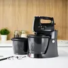 A black hand mixer with two bowls and beaters is displayed on a white countertop with a wooden background. Produktbild-Vorschau