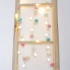 A string of pompom fairy lights is draped over a wooden ladder. Produktbild-Vorschau