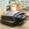 A hand is shown opening a waffle maker with a waffle inside, on a kitchen counter. Podgląd zdjęcia produktu