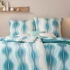 A neatly made bed with a blue and white wave pattern duvet and pillows. Produktbild-Vorschau