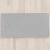 A flat grey shower tray with a drain cover is shown from a top-down perspective, placed on a light-colored wooden floor. Produktbild-Vorschau