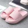 Paar hellrosa Pillow-Slides mit gerippter Riemenstruktur, auf grauer Oberfläche neben Handtüchern und Seifenschale Náhľad obrázku produktu