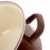 A close-up shot of the handle and rim of a brown and cream enamel pot. Voir les images du produit