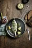 A cooked fish in a pan with lemon wedges and herbs, served on a wooden table with an artichoke, bread, and a bowl of dip. Náhľad obrázku produktu