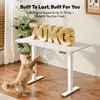 A white standing desk with large gold letters spelling "70KG" on top, and a cat reaching up towards the desk. Produktbild-Vorschau