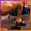 A person is doing push-ups on a paved surface using black push-up bars. Podgląd zdjęcia produktu