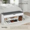 A shoe bench with shoes and boots on it, placed in a bedroom setting next to a bed. Produktbild-Vorschau
