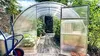 A greenhouse with an open door, showing plants inside and a wheelbarrow outside. Produktbild-Vorschau
