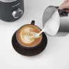 A hand is pouring frothed milk into a cup of coffee, creating latte art. Produktbild-Vorschau