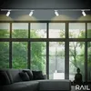 A modern living room with large windows overlooking a lush green forest, featuring a track lighting system, a sectional sofa, and decorative Buddha statue. Náhľad obrázku produktu