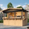 A wooden market stall selling baked goods and coffee, set up outdoors in a paved area with buildings and trees in the background. Voir les images du produit