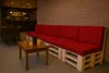 A seating area in a cafe or lounge with a long red pallet sofa and a small wooden table with drinks. Produktbild-Vorschau