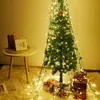 A decorated Christmas tree with lights and presents underneath, next to a small table with books and a photo frame. Náhľad obrázku produktu