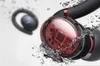Close-up of a transparent earbud showing internal circuitry, with water splashing around it. Produktbild-Vorschau