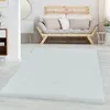 A white rug is laid out on a light gray floor in front of a modern sofa.
