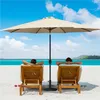 Two people relaxing on lounge chairs under a large umbrella on a sandy beach with the ocean in the background. Produktbild-Vorschau