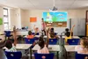 A classroom scene with students raising their hands and a teacher pointing to a diagram on a projector screen. Produktbild-Vorschau