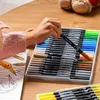 A child's hand is reaching for a marker from a set of art markers, with a coloring book in the foreground. Produktbild-Vorschau