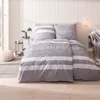 A neatly made bed with grey and white striped bedding, featuring the word "Auszeit" embroidered on the duvet and pillow. Produktbild-Vorschau
