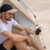 A man is sitting inside a tent, holding a portable Bluetooth speaker. Voir les images du produit