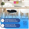 A black ergonomic seat cushion is placed on a white chair in an office setting, with a desk and laptop in the background. Produktbild-Vorschau
