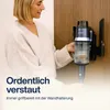 A woman is shown placing a cordless vacuum cleaner onto its wall-mounted charging station. Produktbild-Vorschau