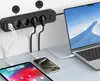A black power strip with multiple outlets and USB ports is mounted on a white wall, with various electronic devices plugged in and charging. Anteprima dell’immagine prodotto