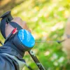 A person's hand holding a dog leash with a blue device attached, outdoors in a park. Podgląd zdjęcia produktu