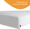 A close-up view of a white mattress with a purple tag on the corner, set against a white background with an orange overlay containing text. Produktbild-Vorschau