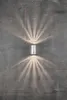 A silver cylinder-shaped wall light fixture mounted on a textured gray concrete wall, casting fan-shaped light patterns upwards and downwards. Anteprima dell’immagine prodotto