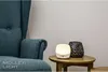 A teal armchair sits next to a small wooden side table with a white LED night light and a black decorative vase on it. Produktbild-Vorschau