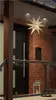 A star-shaped LED light is hanging above a front door, next to a brick wall and a glass railing. Produktbild-Vorschau
