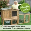 A young girl stands behind a wooden rabbit hutch with an attached run, smiling with her arms outstretched. The hutch is on a grassy lawn. Produktbild-Vorschau