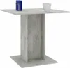 A square dining table with a concrete gray finish and a pedestal base, shown against a white background. Two white cups and a blue object are placed on the table. Náhľad obrázku produktu