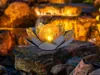 A glowing orb sits in a lotus-like holder on rocks, with a blurred waterfall in the background. Produktbild-Vorschau