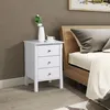 A white nightstand with three drawers is placed next to a bed with a wooden headboard. Produktbild-Vorschau