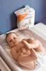 A baby lying on a changing mat with a pack of baby wipes in the background. Voir les images du produit