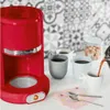 A red coffee maker is shown on a counter with several mugs being filled with coffee. There is also a jar of sugar cubes in the background. Anteprima dell’immagine prodotto