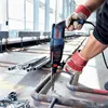 A person is using a Bosch hammer drill to drill into a metal pipe on a construction site. Náhľad obrázku produktu