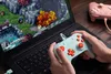 A person is playing a video game on a laptop using a mint-colored controller, with another pink controller visible in the background. Produktbild-Vorschau