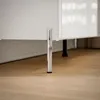 A close-up shot of the bottom of a white cabinet with a silver chrome leg on a wooden floor. Produktbild-Vorschau