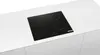 A black induction hob is embedded in a white countertop. Voir les images du produit