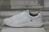 A white leather sneaker is shown from the side against a wood-paneled background. Náhľad obrázku produktu