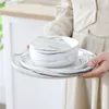 A person holding a set of marble-patterned dishes. Produktbild-Vorschau